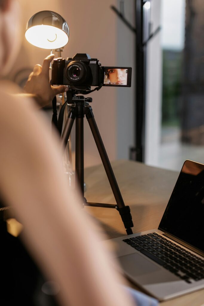A person sets up a DSLR camera on a tripod for vlogging indoors, illuminated by a lamp.